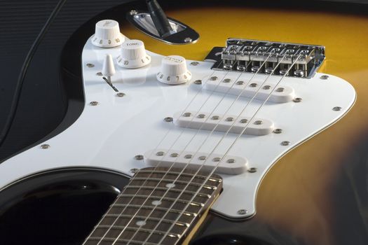 Closeup of electric guitar Stratocaster-type, white and sunburnt, with strings