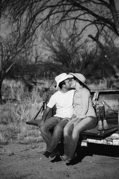 Man and woman in cowboy hats kissing on back of pickup truck
