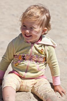 Cute little European toddler girl having fun with sand on the beach.