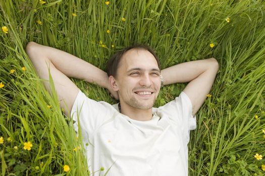 The man lies on a grass and smiles