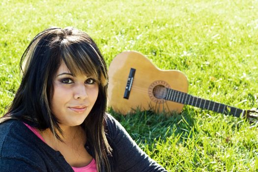 A young woman sitting in the green grass with an acoustic guitar in the background. Shallow depth of field.