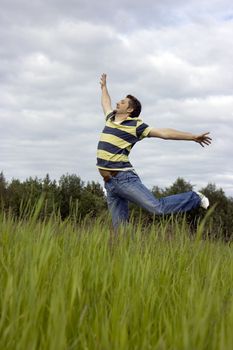 The young man joyfully jumps on a grass