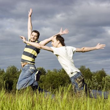 Two young men joyfully jump on a grass