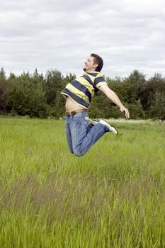 The young man joyfully jumps on a grass