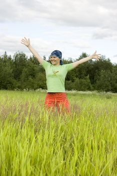 The girl in bright clothes costs in a grass having stretched hands