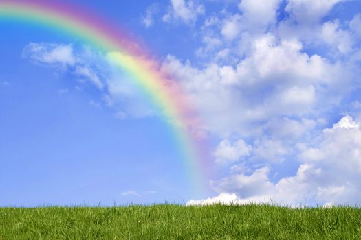 Beautiful green grass against blue sky and rainbow.