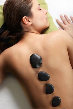 young woman lying on a massage table. hot stone massage stones lying on her back
