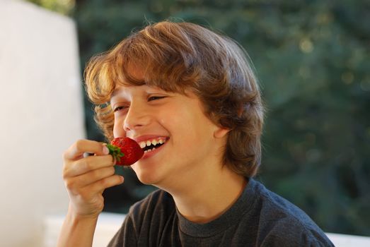 Smiling teenage boy about to bite a strawberry.