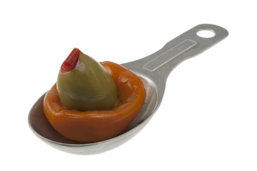 olive stuffed with pimento and orange marinated pepper on an old aluminum measuring tablespoon isolated on white