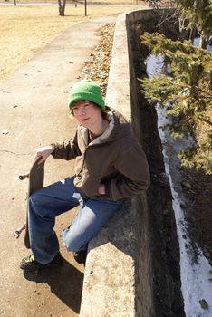 A young teen boy sits on a concrete ledge with his skateboard.