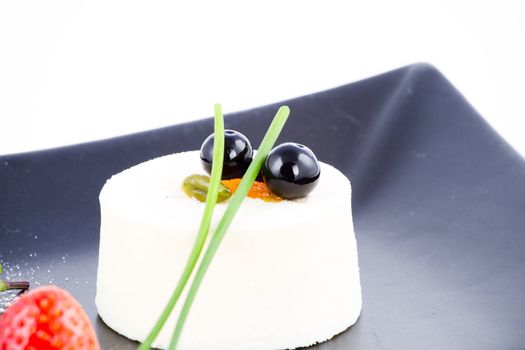 Vanilla mousse dessert on square black plate with cranberries