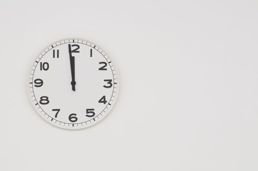 White clock with black hands showing one minute to midnight, noon