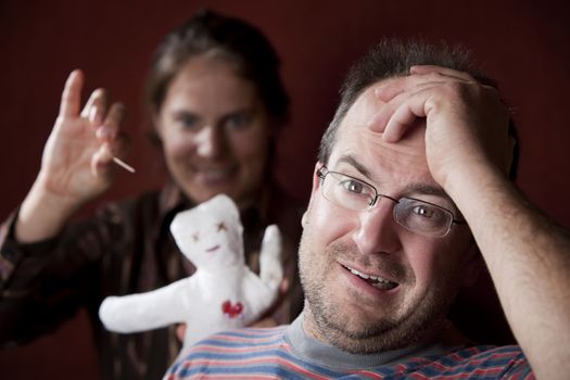 Guilty man with upset woman poking voodoo doll in the background