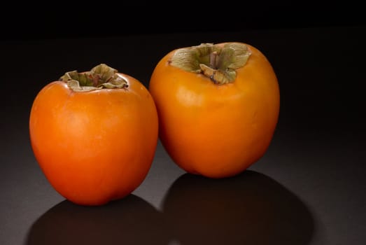 Two fresh ripe persimmons on black background