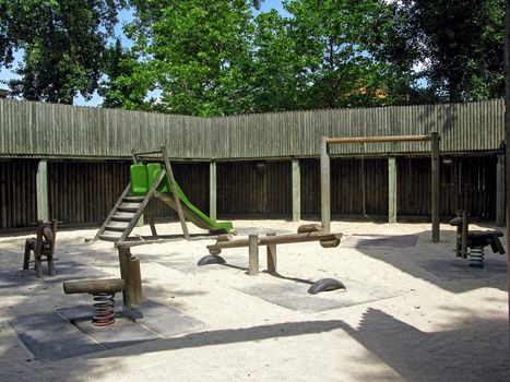 A playground in the middle of a forest, in a fort with sand on the ground.
