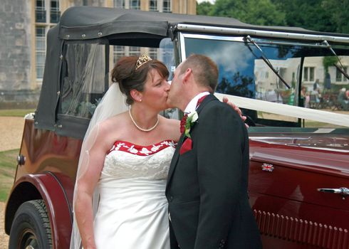 Bride and Groom kissing in front of their wedding car