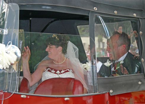 Bride and Groom sitting in Wedding Car Waving