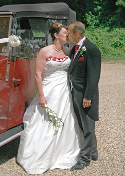 Bride and Groom Kissing in front of their Wedding Car