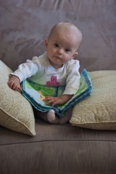 Little baby girl sitting on a sofa and playing with cloth book.