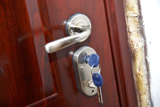 brown front door with silver metallic handle and hanging keys in lock