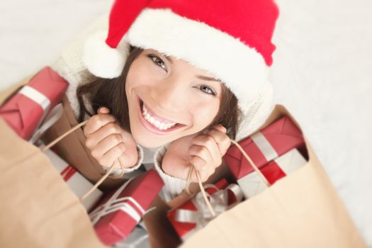 Woman shopping for christmas gifts. Young asian caucasian girl looking up smiling with shopping bags and santa hat. Copy space on the side.