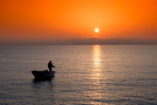 Man in a boat angling at sunset
