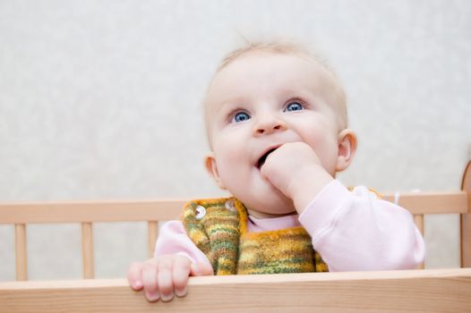 Curious baby with finger in mouth standing in bed