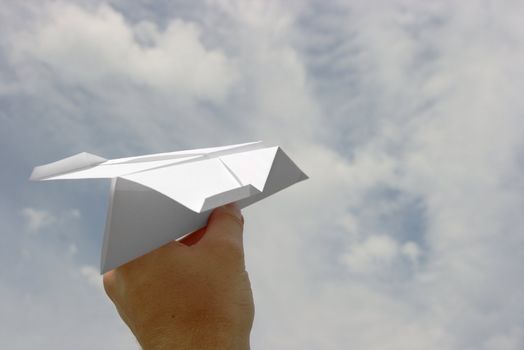 Paper plane in a hand against cloudy sky