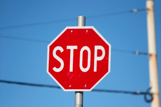 Red stop sign under clear blue sky, wires in the background, urban environment