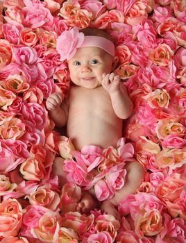 Adorable smiling baby girl lying in a bed of pink roses 