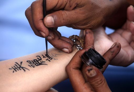 Artist draws a tattoo henna on a female hand. Hieroglyph "Beautiful dream"