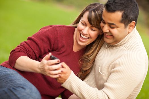 Attractive Mixed Race Couple Enjoying Their Camera Phone in the Park.