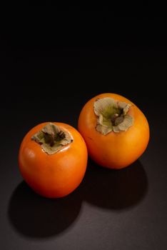 Two freshly picked persimmons, still life on black