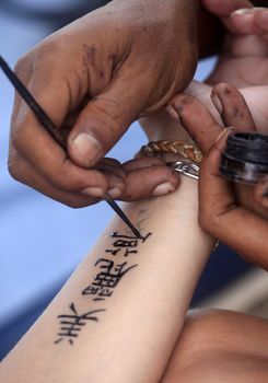 Artist draws a tattoo henna on a female hand. Hieroglyph "Beautiful dream"