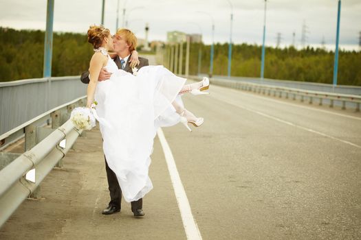 The groom carries his bride in his arms on the bridge