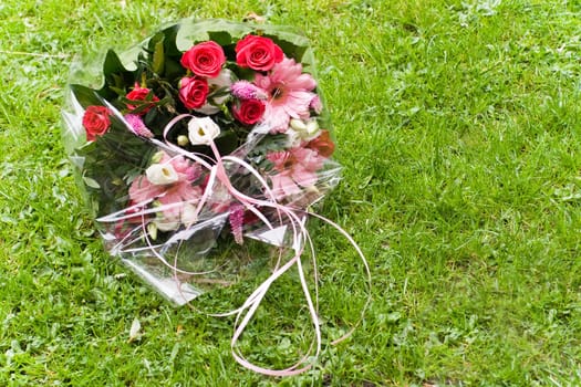 Bouquet of red, pink and white flowers from florist laying on field of grass