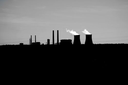 Nuclear Power Plant Silhouette captured in Florida in the United States. Steam or Smoke is shown coming from the top of the stacks which are on the horizon. There is plenty of copy space on both the black foreground and across the grey sky backgound.

