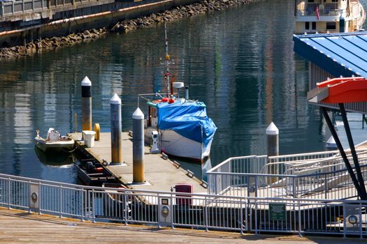 Boats Moored at Pier in Seattle show a couple of small boats tied up at the docks with many beautiful reflections showing across the water in this beautiful waterfront composition. A fence frames the immediate foreground.
