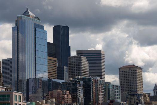 Downtown Seattle v1 buildings and skyscrapers are captured against a cloudy sky which is typically generated from being on the coast of Puget Sound Washington. There are beautiful reflections in the buildings. The buildings look like steps up or building blocks in the amazing piece of architecture landscape.
