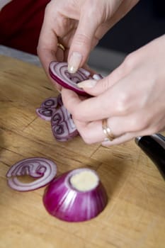 A woman cutting vegetables at home on the counter. A shallow depth of field is used to bring the hands and red onion in to attention.