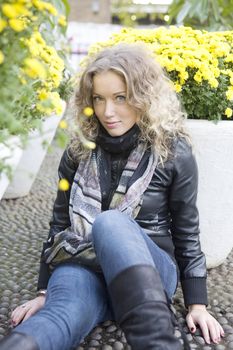 portrait of young attractive blond girl with curl hair sitting on the stone-block pavement between two vase of flower in the park