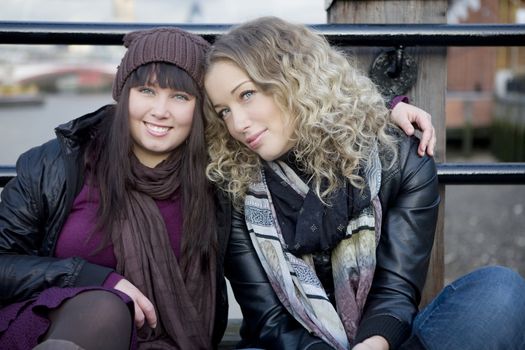 portrait of attractive embracing girls sitting on the bridge. London