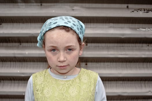 young girl wearing head scarf and green jumper dress against steel door