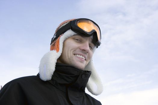 The young man in ski glasses and a winter cap against the sky