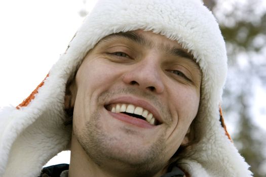 The young man in a winter cap against the sky and wood