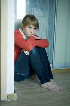 young sad girl sitting on corner in room. Teen`s problem