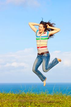 A beautiful young woman jumping up in the air laughing outdoors by a beautiful ocean