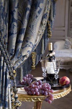 Curtain and bottle of vine with grape standing on table 