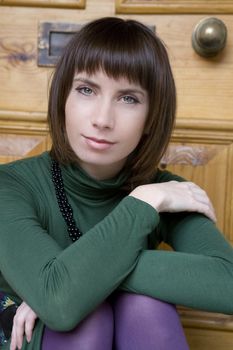 portrait attractive brunette pensive woman with beads wearing green blouse
 at door 
