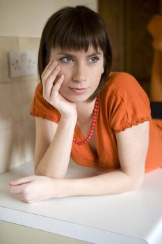 Young attractive woman in orange shirt and red beads lying on table in kitchen. Five minutes for reflection